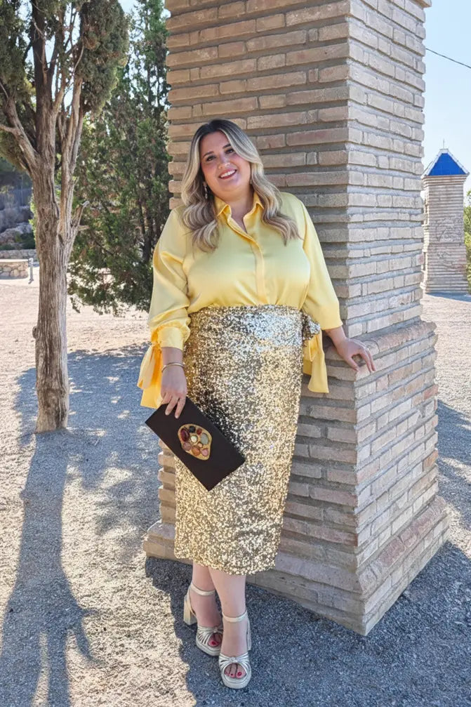 Chica rubia de talla grande con camisa amarilla con lazos de talla grande. Look de fiesta.