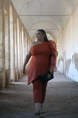 Modelo talla grande luciendo un conjunto de color teja. Top con escote asimétrico y manga abullonada de seda color teja.