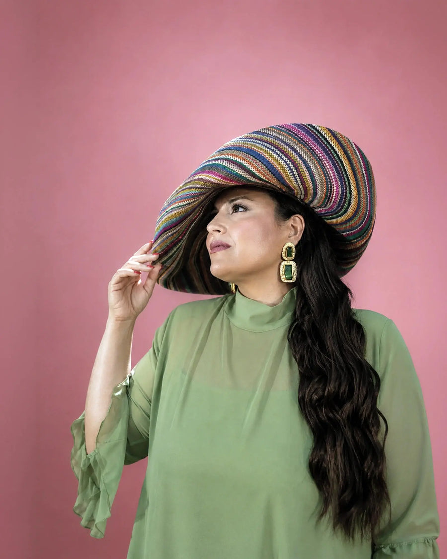 Detalle del vestido Marina de gasa verde salvia combinado con pamela de rafia multicolor, modelo sujetando el ala del sombrero, talla grande