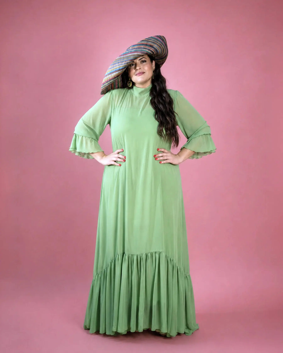 Vestido Marina de gasa verde salvia con volantes en bajo y mangas, pose con manos en la cintura y pamela multicolor, talla grande