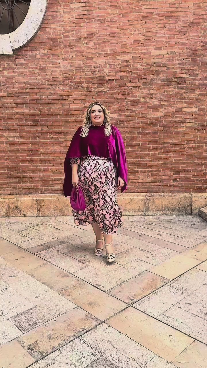 "Vídeo de mujer con curvas luciendo capa de terciopelo fucsia en talla grande, combinada con vestido de fiesta estampado y bolso a juego – look elegante Corintia